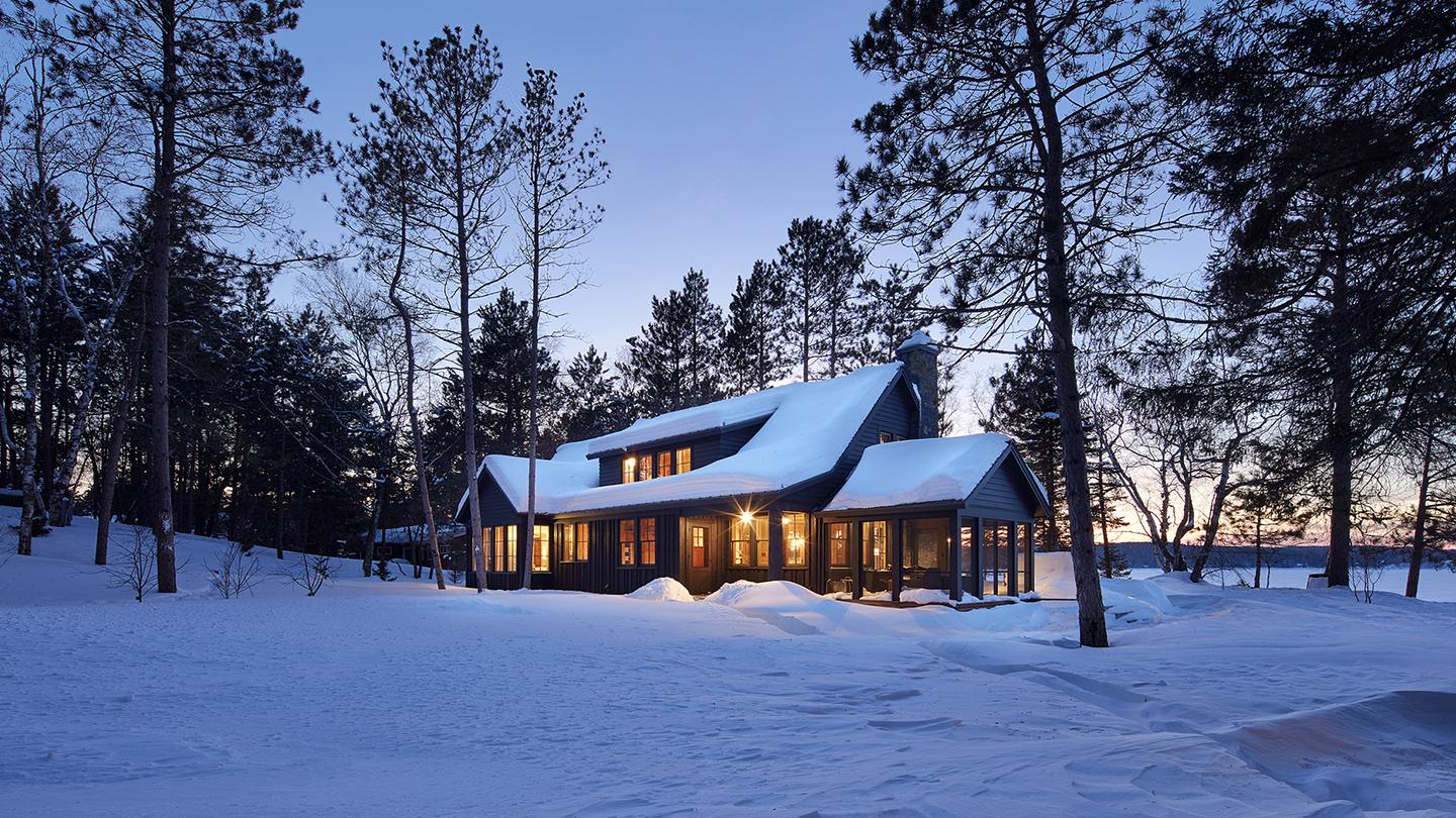 A snow-covered Minnesota house at dusk, windows glowing